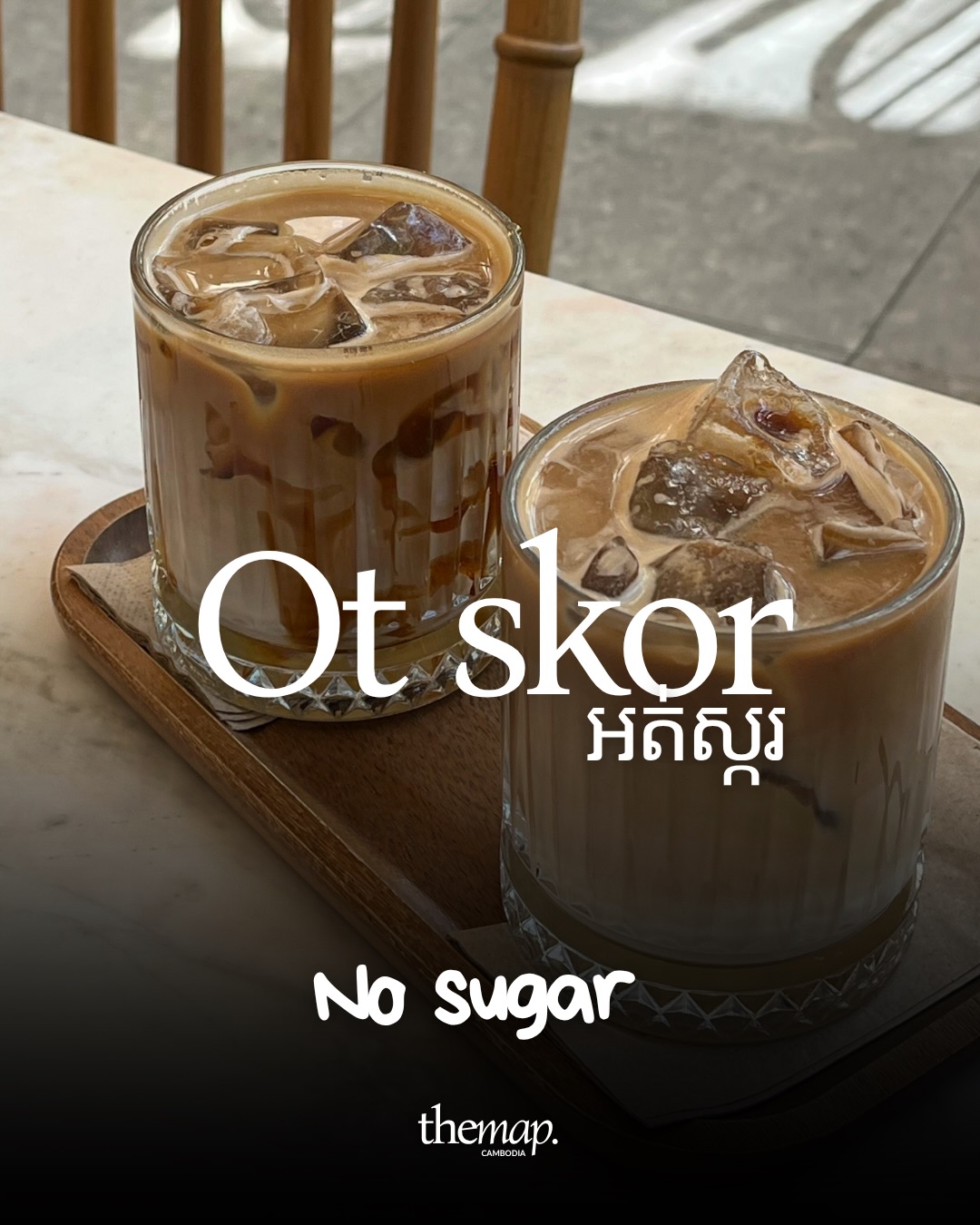 Deux verres de café glacé sur un plateau en bois posé sur une table en marbre, accompagnés de l'expression khmère pour sans sucre